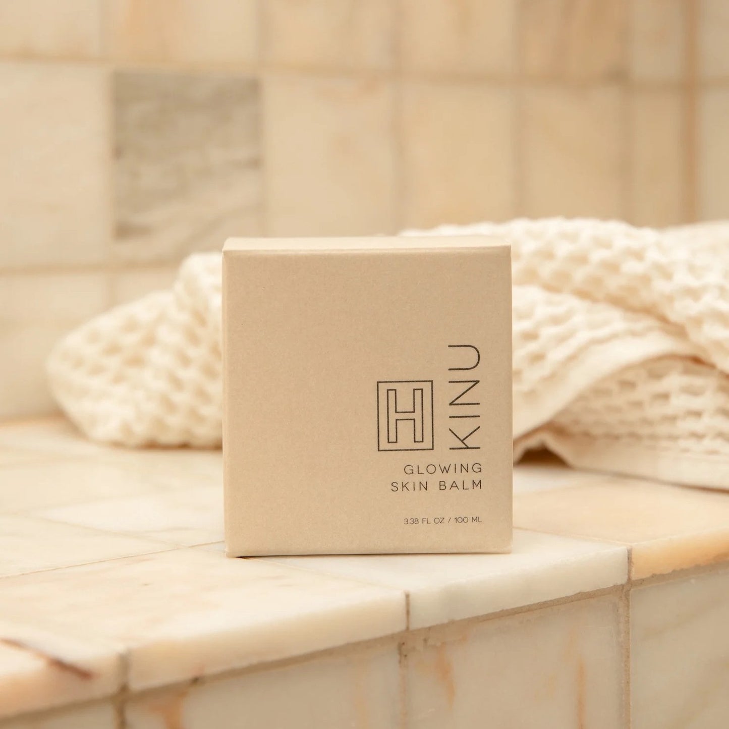 Kinu Glowing Skin Balm box on a marble surface with a towel in the background