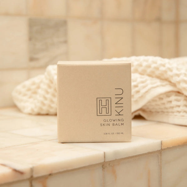 Kinu Glowing Skin Balm box on a marble surface with a towel in the background