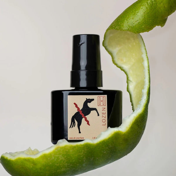 Black perfume bottle with a label on a sliced lime background