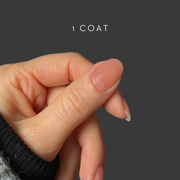 Close-up of a hand with a single applied coat of nail polish on a dark background. HELLO TOMATO Djamor