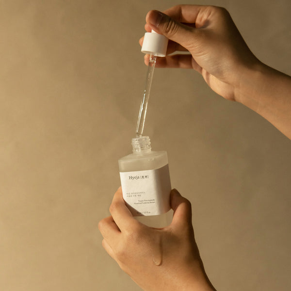 Hand holding a dropper bottle with a beige background