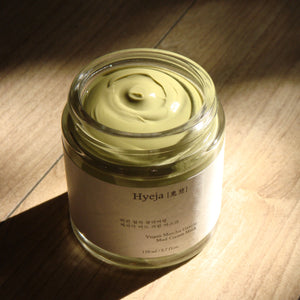A clear glass jar of HYEJA Vegan Matcha Gentle Mud Cream Mask