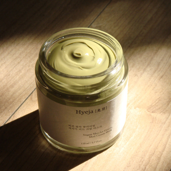 A clear glass jar of HYEJA Vegan Matcha Gentle Mud Cream Mask