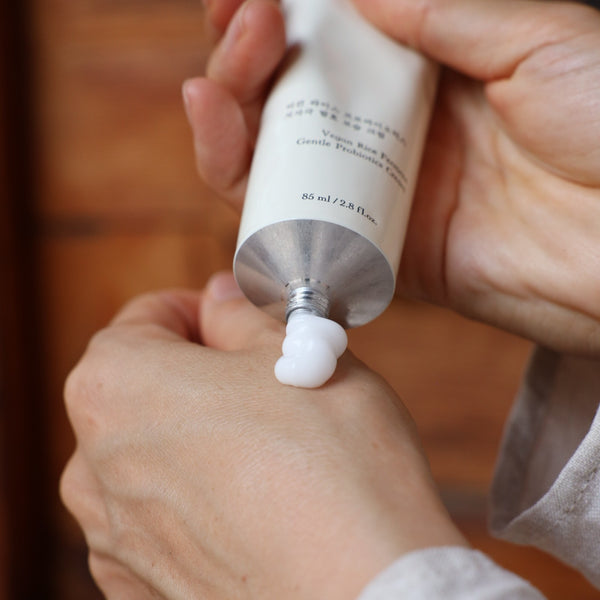 Person applying white cream from a tube onto their hand against a blurred background