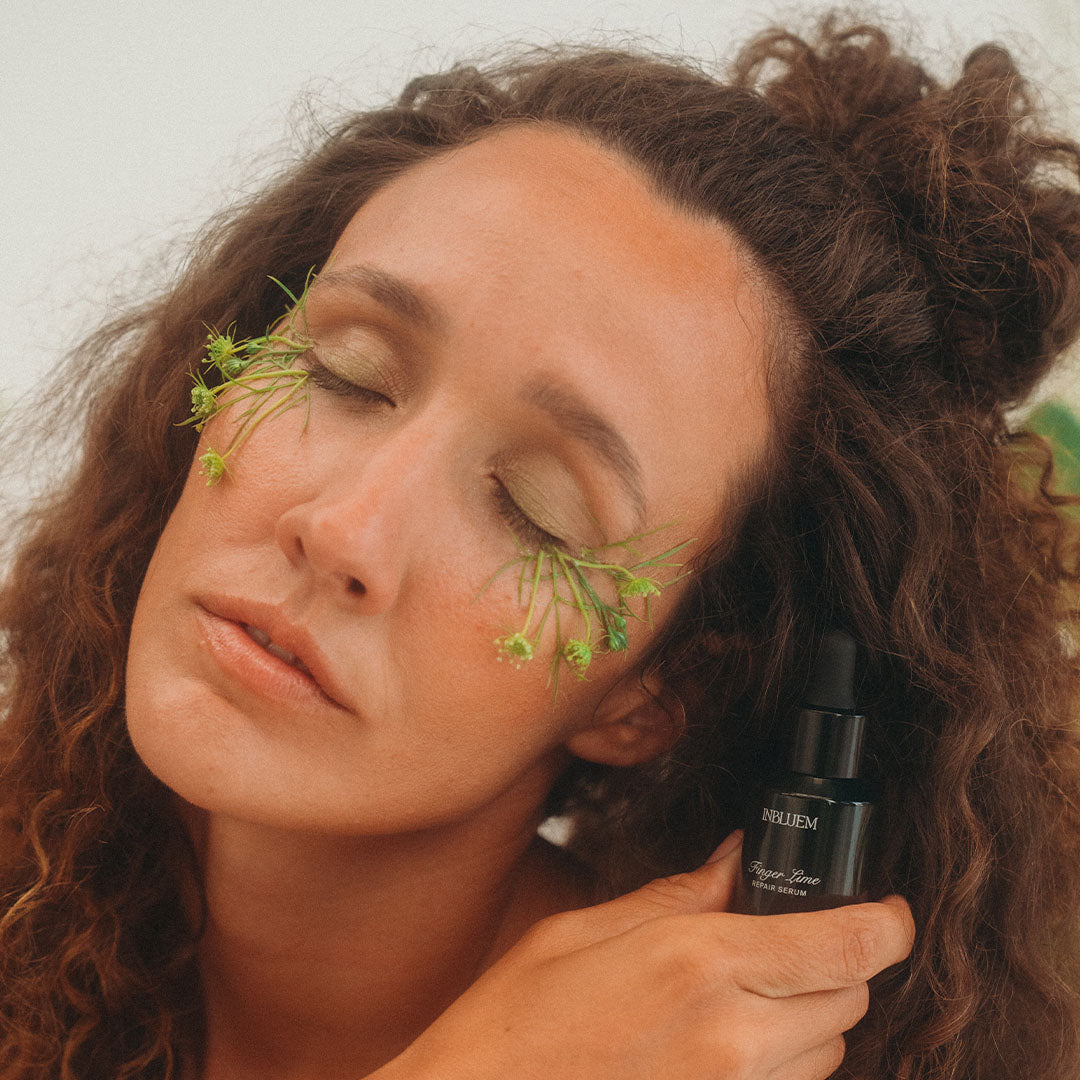 Woman with green leaves on her face holding a skincare bottle. INBLUEM Finger Lime Serum
