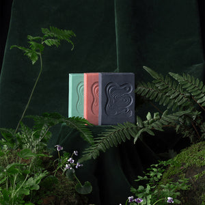 Three soap bars in green, red, and light black on a dark background with ferns and plants. INBLUEM Soul Soap Charcoal & Lemon Myrtle