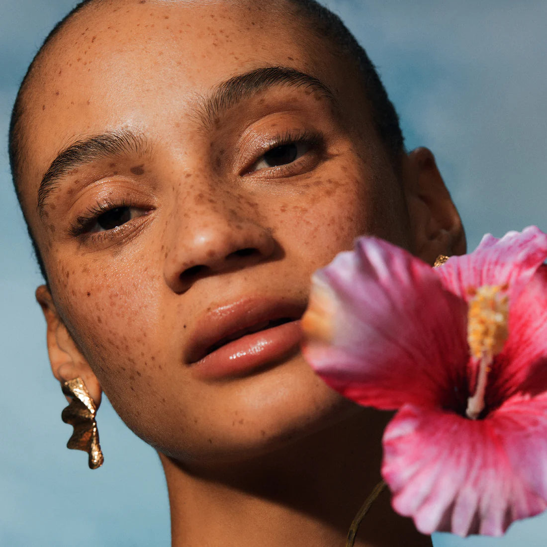 Close-up of a woman with a pink flower in front of their face against a blue background