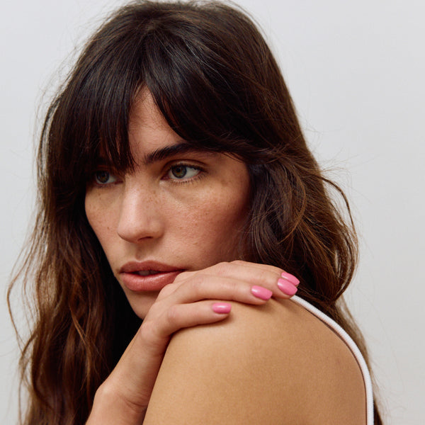 Woman with long brown hair and pink nail polish resting her head on her hand against a plain background