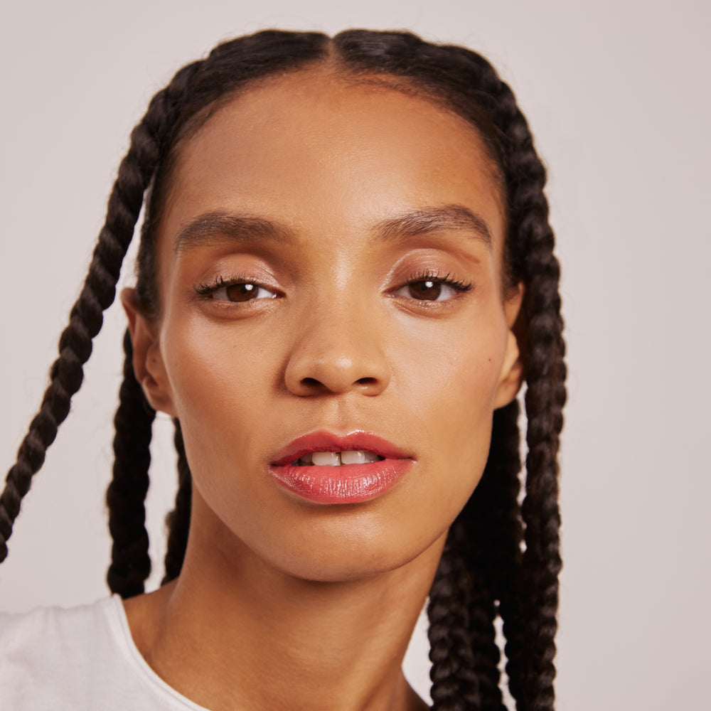 A tube of Karolin Van Loon lip gloss in Honey, featuring a vibrant coral shade that captures the essence of a sun-drenched summer day. This gloss delivers a bright sheen while enhancing the lips with a subtle tint, providing a smooth, non-sticky, and hydrating effect for fuller, voluminous lips.