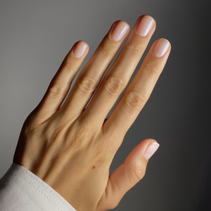 Close-up of a hand with light off white nail polish on a dark background