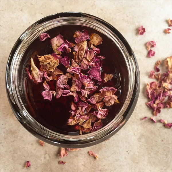 Jar of dark liquid with dried flowers on a beige surface. LEPAAR Harmony Rose Serum / Face + Neck Oil