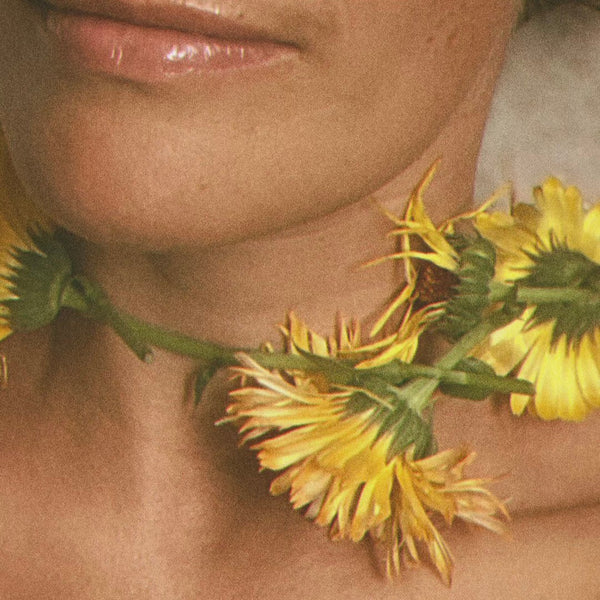 Close-up of a woman with yellow flowers around her neck. LEPAAR Luminous Beauty Balm / Ultra Restorative Moisture Lock