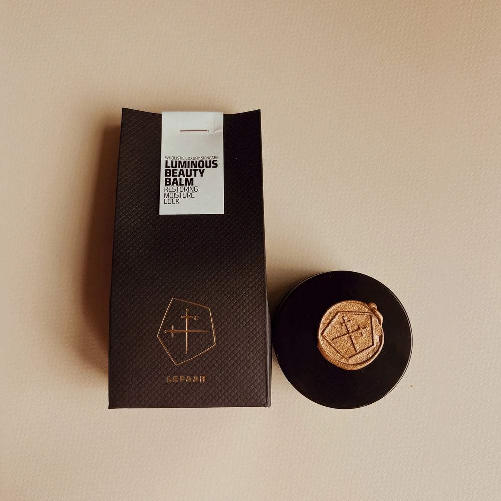 Round black object with a gold emblem on a white background. LEPAAR Luminous Beauty Balm / Ultra Restorative Moisture Lock