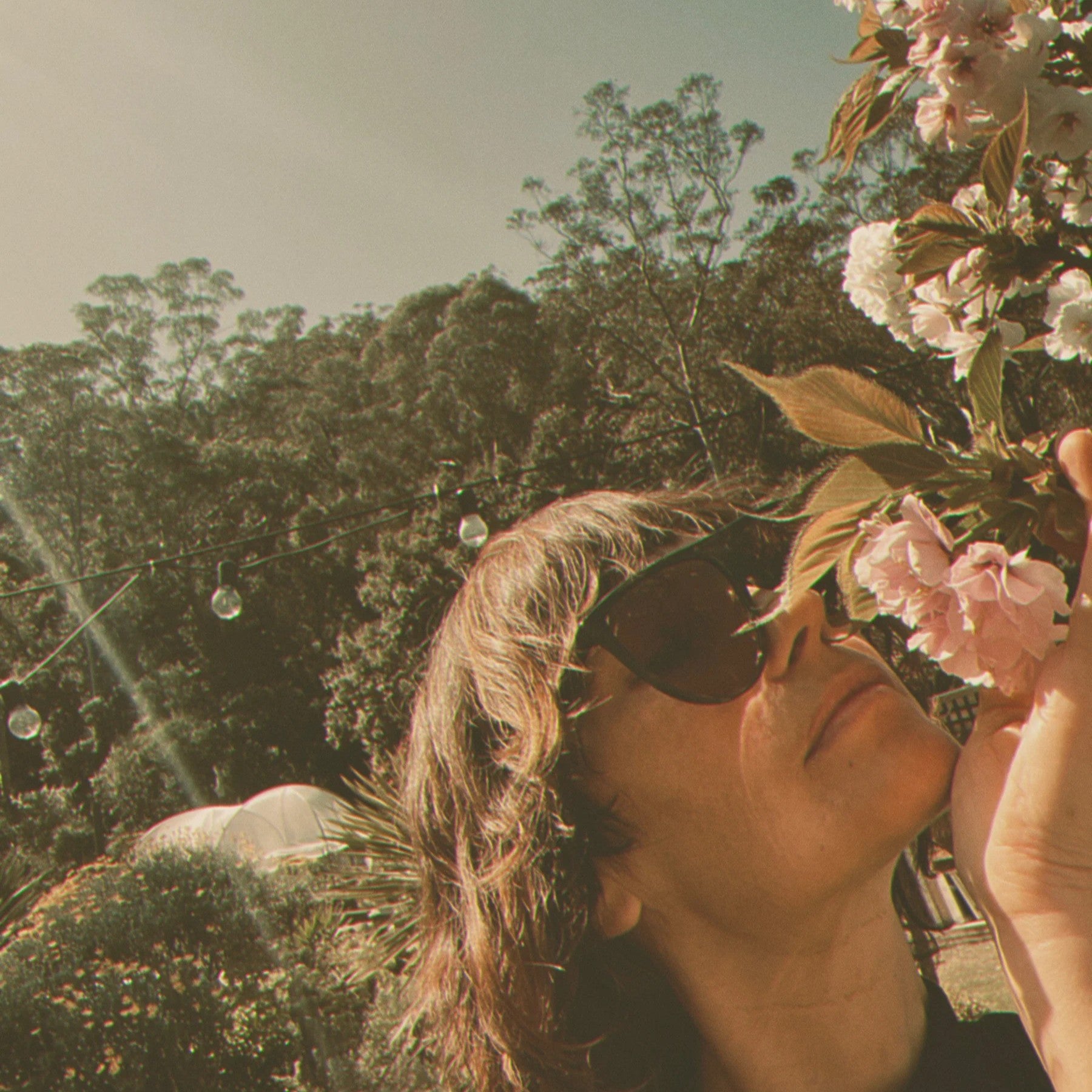 A woman with sunglasses smelling flowers with a scenic background
