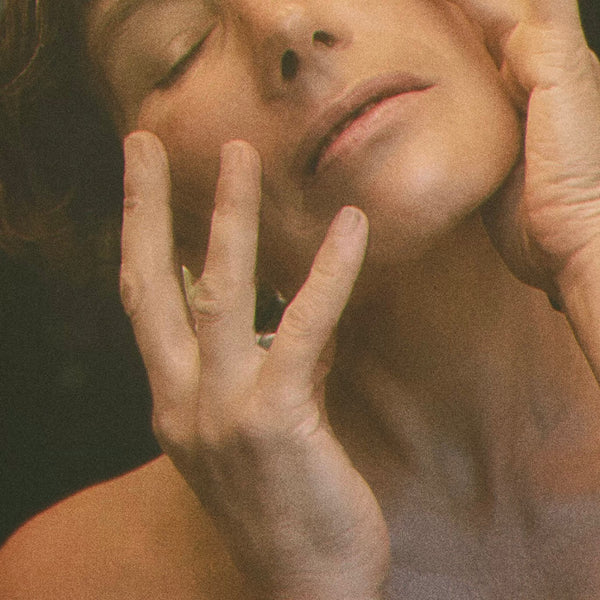 Close-up of a woman's face with hands on her cheeks, against a dark background. LEPAAR Serenity Evening Balsam