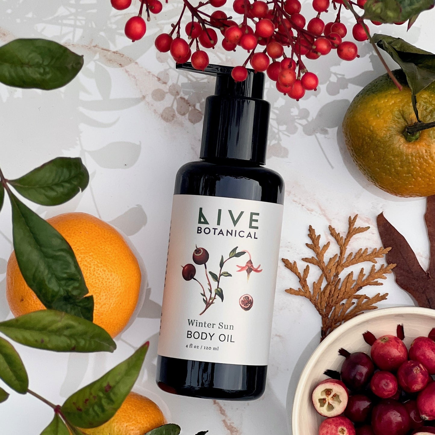 LIVE Botanical winter sun body oil bottle surrounded by fruits and leaves on a light background