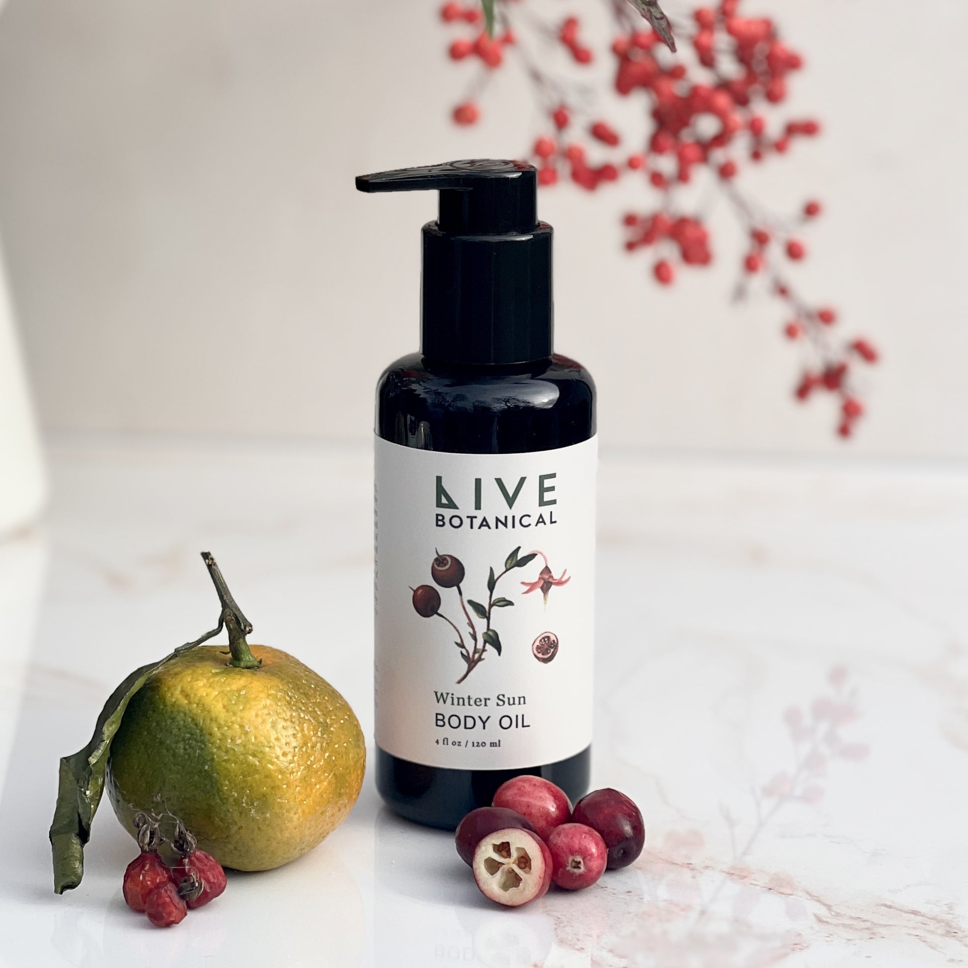 Bottle of Live Botanical Winter Sun Body Oil with an orange and berries on a light background