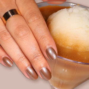 Close-up of hands with shimmering brown nail polish holding a glass of iced coffee.