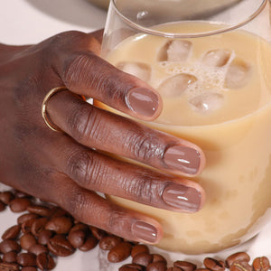Hand holding a glass of iced coffee with coffee beans on a white background