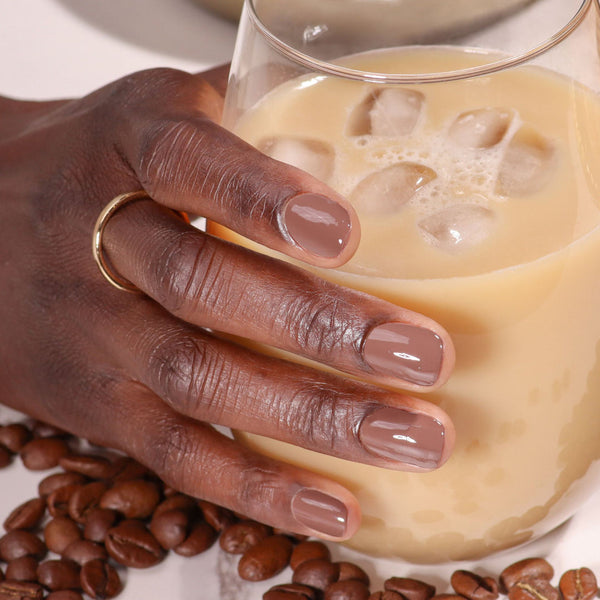 Hand holding a glass of iced coffee with coffee beans on a white background