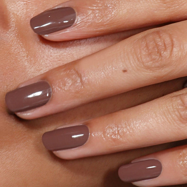 Close-up of a hand with brown nail polish on a neutral background