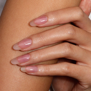 Close-up of a hand with sheer pinkish nail polish on a light skin background