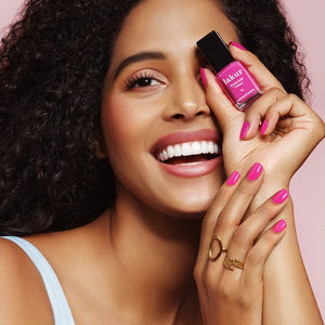 Woman holding a bottle of pink nail polish with a pink background