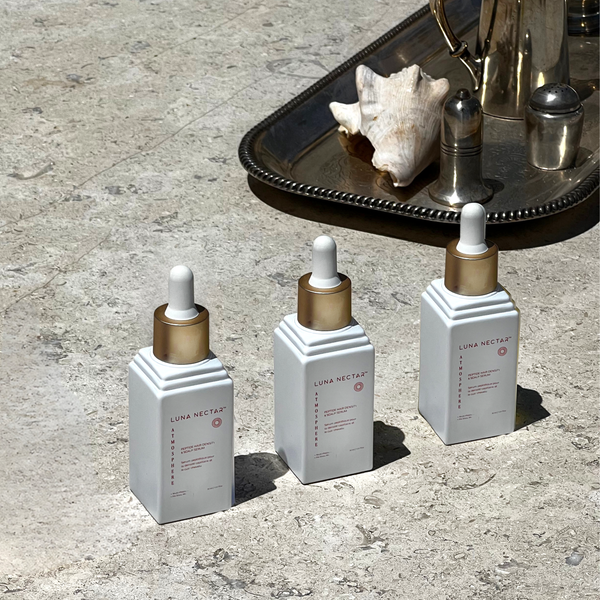 Three skincare dropper bottles labeled 'Luna Nectar' on a textured surface with a shell and metallic container in the background.