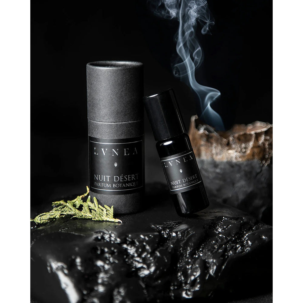 LVNEA Nuit Désert perfume in a 10ml amethyst glass bottle with a roller ball applicator, featuring a blend of cedar leaf, smoke, vetiver, and other earthy notes, encased in a matte black tube.