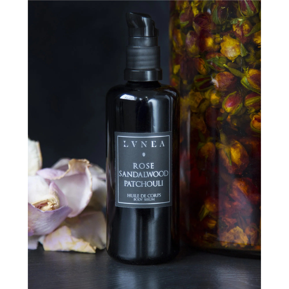 LVNEA Rose Sandalwood Patchouli Floral Body Serum: A luxurious 100ml body oil in an amethyst glass bottle with a pump dispenser. Infused with rose extracts, sandalwood, and patchouli, it offers deep moisture and a soft, enchanting fragrance. Handcrafted in small batches.