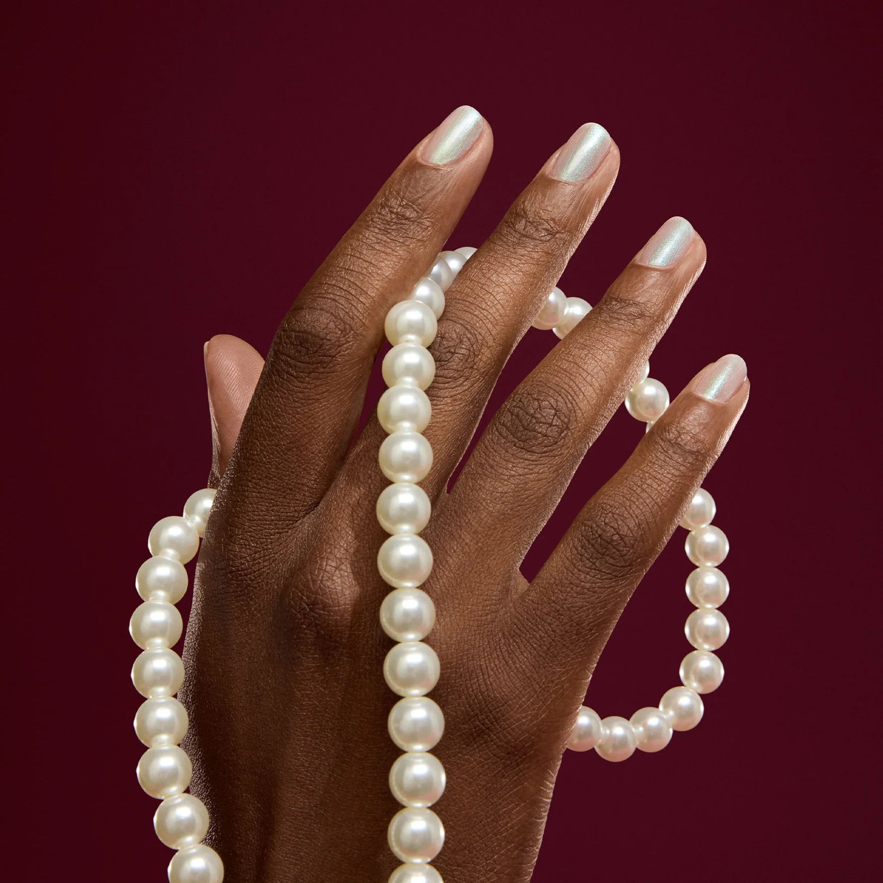Hand holding a pearl necklace against a red background