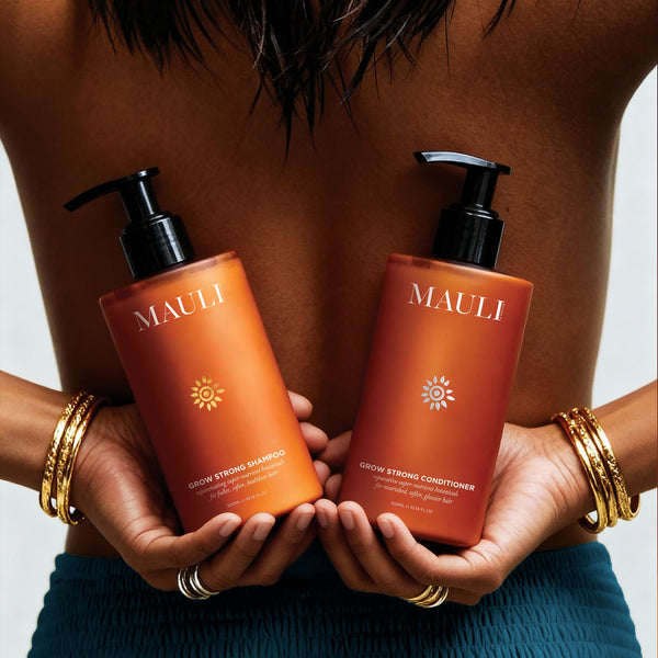 Two bottles of Mauli Rituals Grow Strong Shampoo and Conditioner held by a person with gold bracelets.