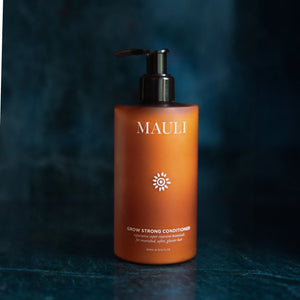 Brown/amber colored bottle of MAULI conditioner on a dark textured background