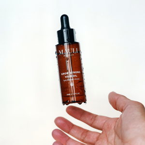 Brown hair oil dropper bottle held by a hand against a white background