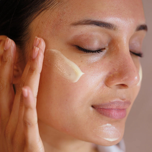 Woman applying cream to her face with a neutral background