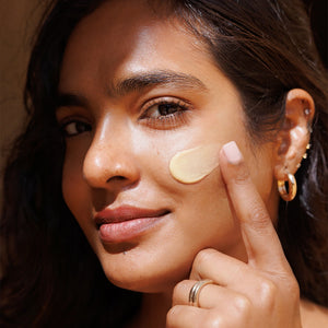 Woman applying cream to her face with a close-up focus on her skin texture.
