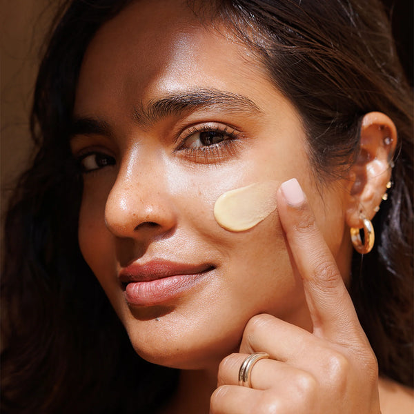 Woman applying cream to her face with a close-up focus on her skin texture.