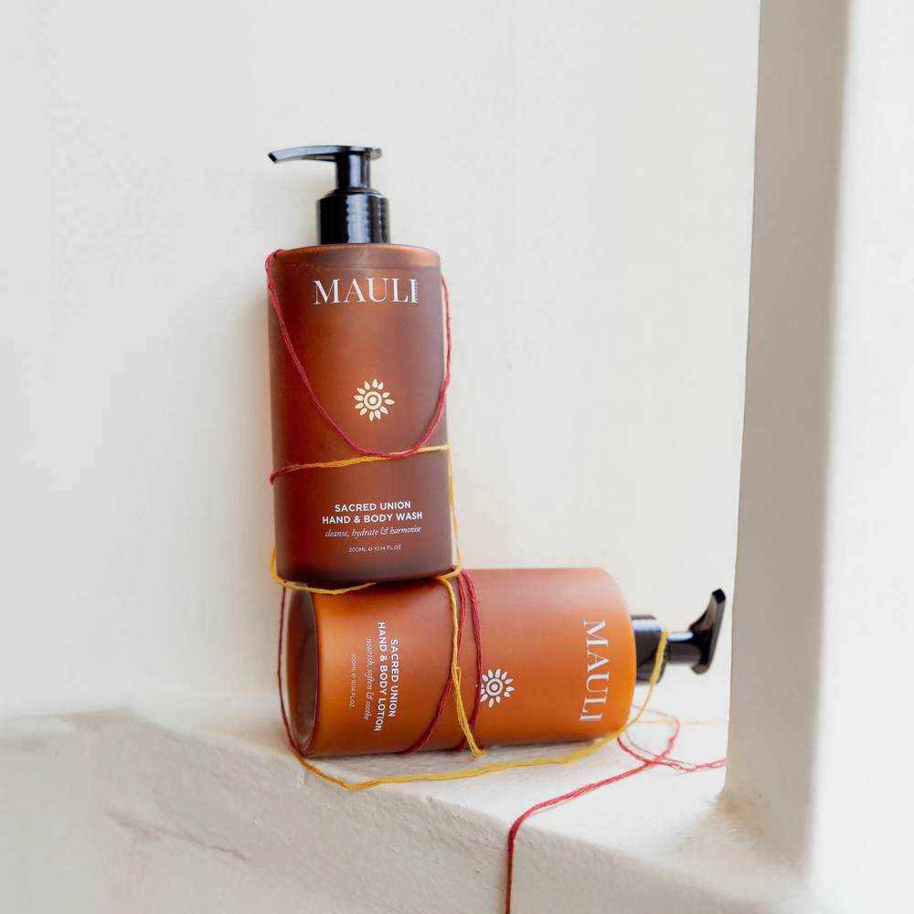 A dark orange bottle of MAULI RITUALS Sacred Union Hand & Body Lotion with black pump on white background