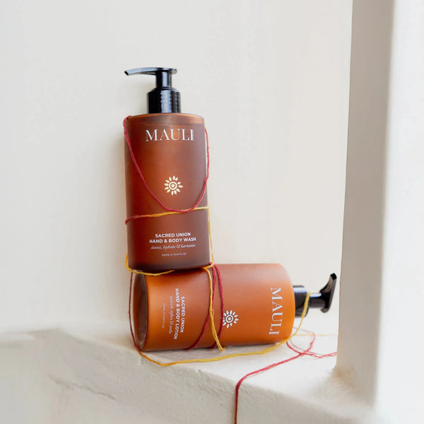 Two bottles of Mauli Rituals hand and body wash stacked on a white surface with a neutral background.