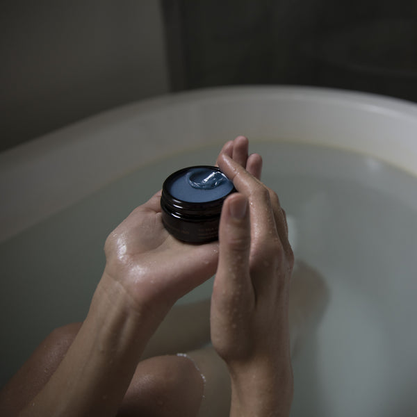 Person holding a jar of blue balm over a bathtub