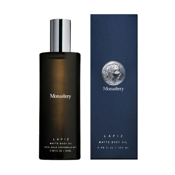 Lapiz matte body oil from Monastery in glass bottle with silver cap and box next to it on white background
