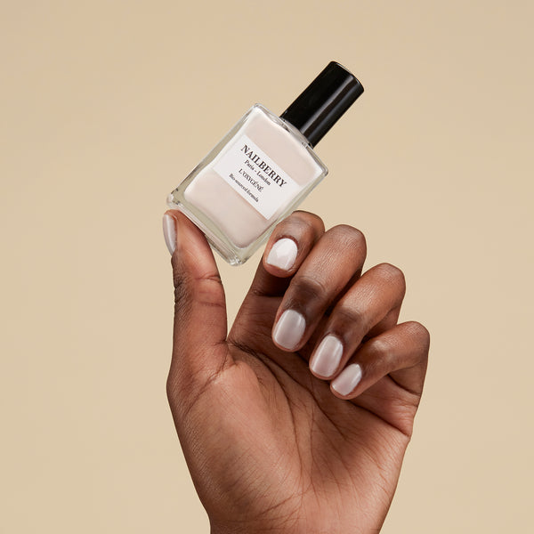 Hand holding a bottle of Nailberry nail polish against a beige background
