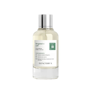 A bottle of Olfactory X Bergamot + Leaf 100% natural perfume with a clear glass body, light yellow liquid, a white label with green accents, and a reflective silver cap, set against a plain white background.