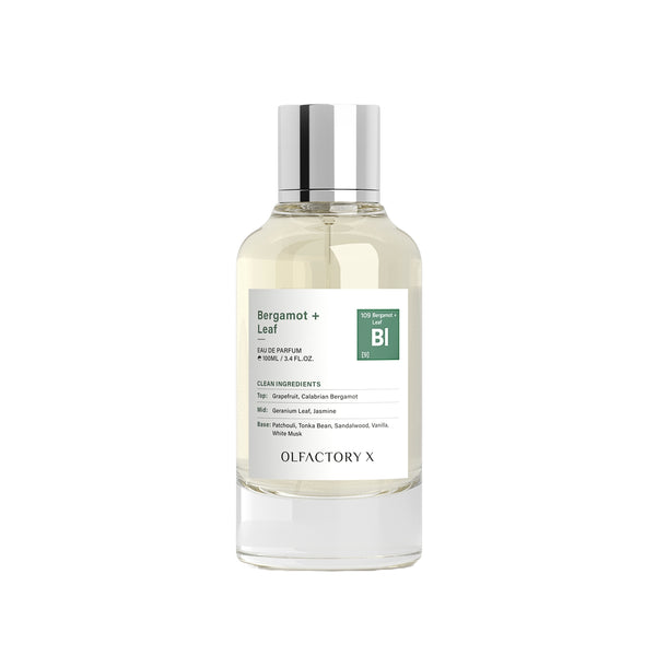 A bottle of Olfactory X Bergamot + Leaf 100% natural perfume with a clear glass body, light yellow liquid, a white label with green accents, and a reflective silver cap, set against a plain white background.