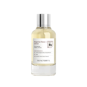 A clear glass bottle of Olfactory X Bulgarian Rose + Velliver Eau de Parfum with a silver cap, containing a pale yellow liquid, set against a plain white background.