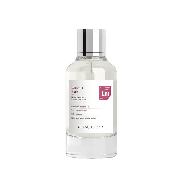 A clear glass bottle of Olfactory X Lemon + Musk Eau de Parfum with a reflective silver cap and a white label, set against a plain white background.