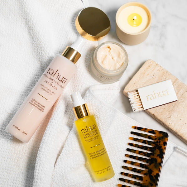 Haircare products including a bottle, serum, and candle on a textured surface with 'rahua' branding.