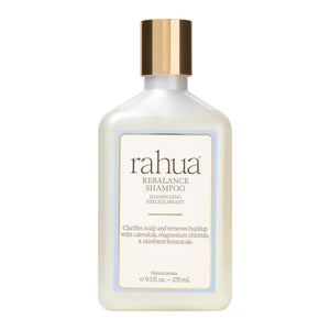 A bottle of Rahua Rebalance Shampoo with a frosted off-white body, a metallic gold cap, and a cream-colored label with a light blue border, set against a plain white background.