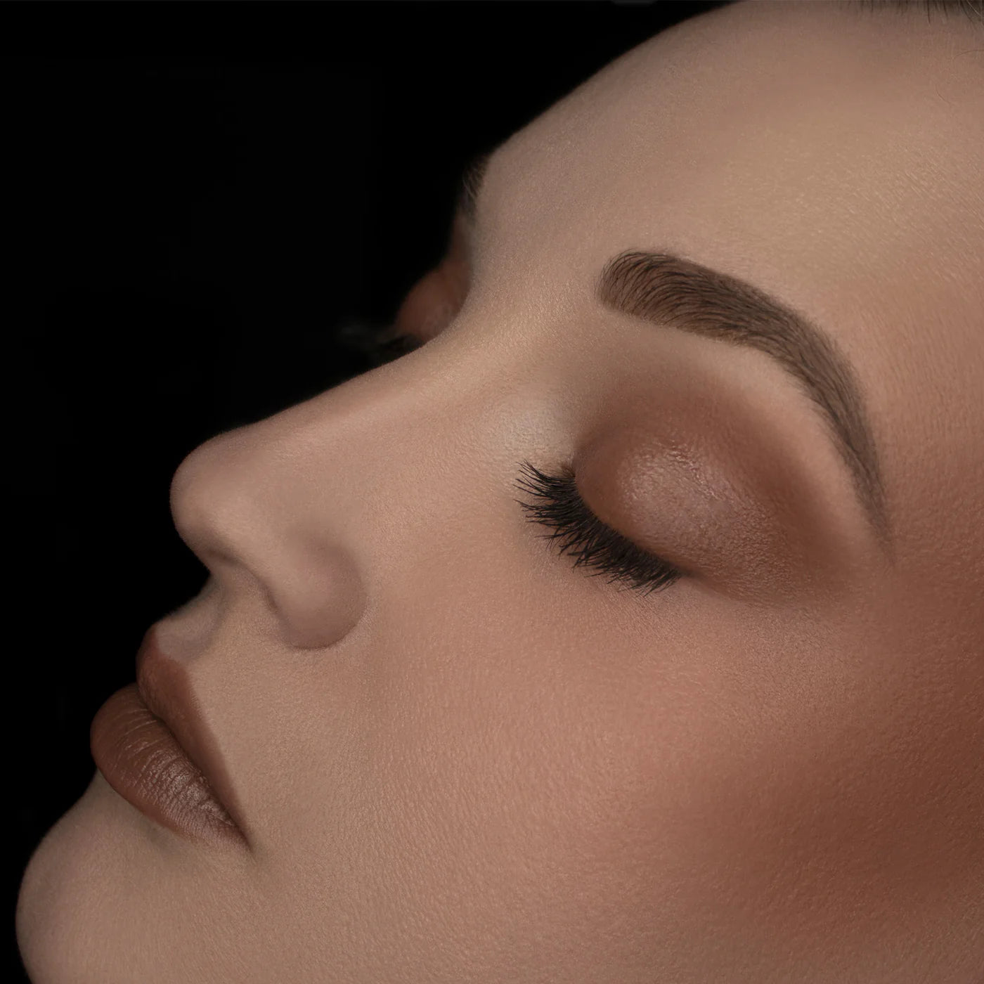 Close-up of a person's face with closed eyes on a black background. RITUEL DE FILLE Inner Glow Crème Pigment Eros
