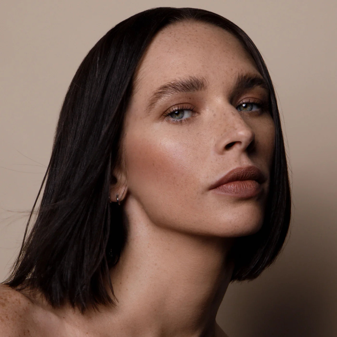 Close-up of a woman with shorter dark hair against a neutral background. RITUEL DE FILLE Inner Glow Crème Pigment Eros